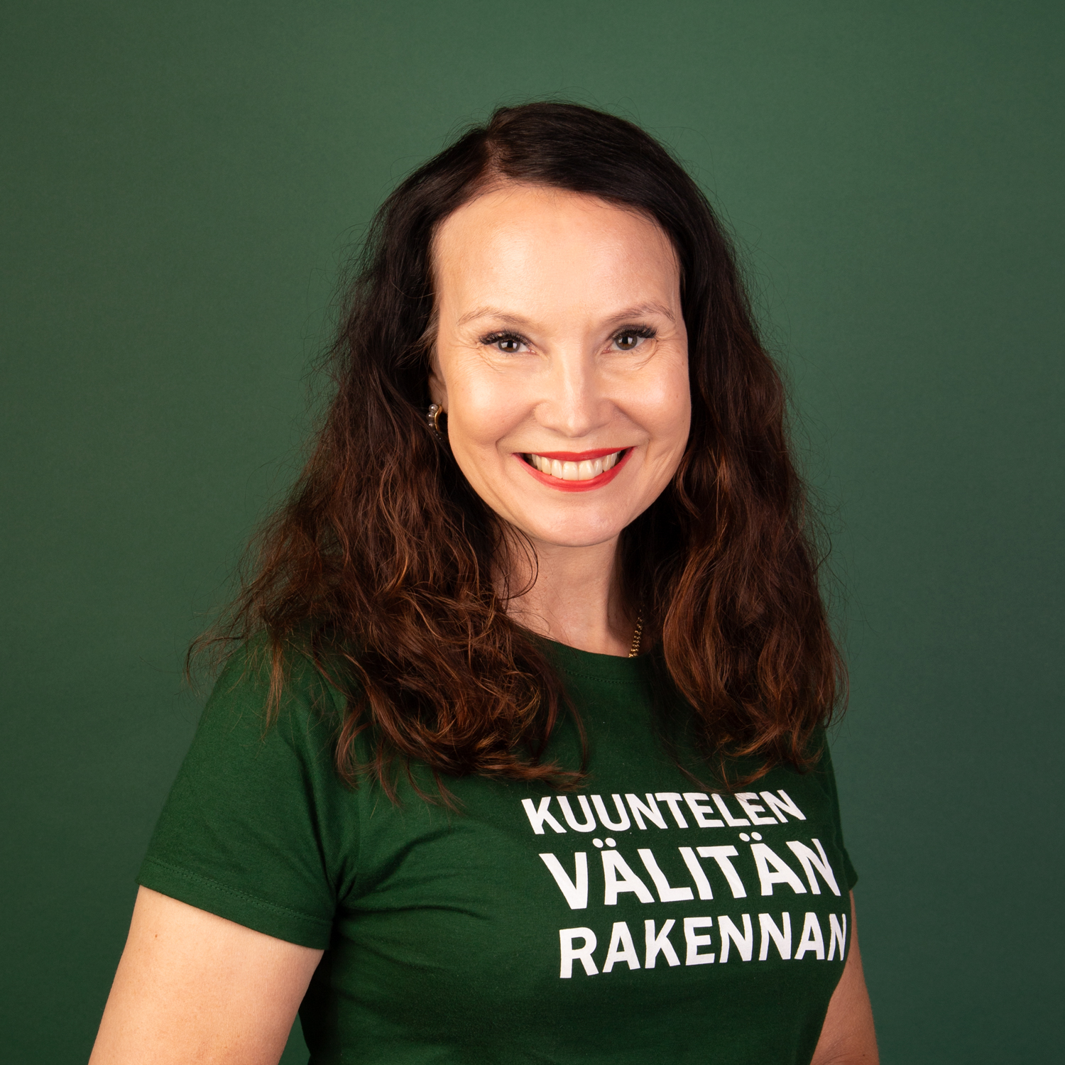 Johanna Rantalainen studiokuvassa. Vihreä tausta ja T-paidassa teksti: kuuntelen, välitän, rakennan.