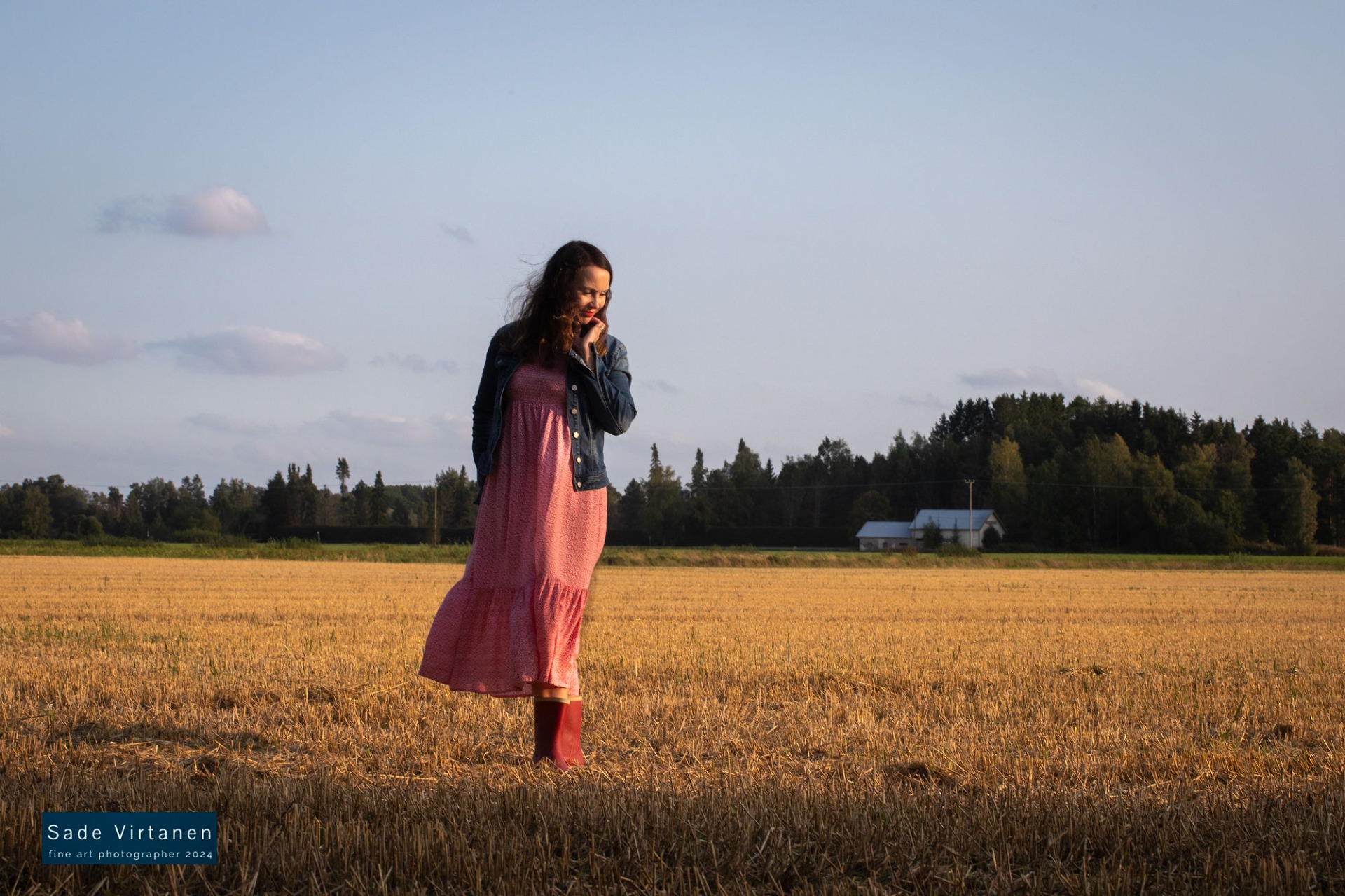 Johanna Rantalainen satakuntalaisella pellolla auringonlaskun valossa, punainen mekko ja punaiset saappaat sekä farkkutakki.
