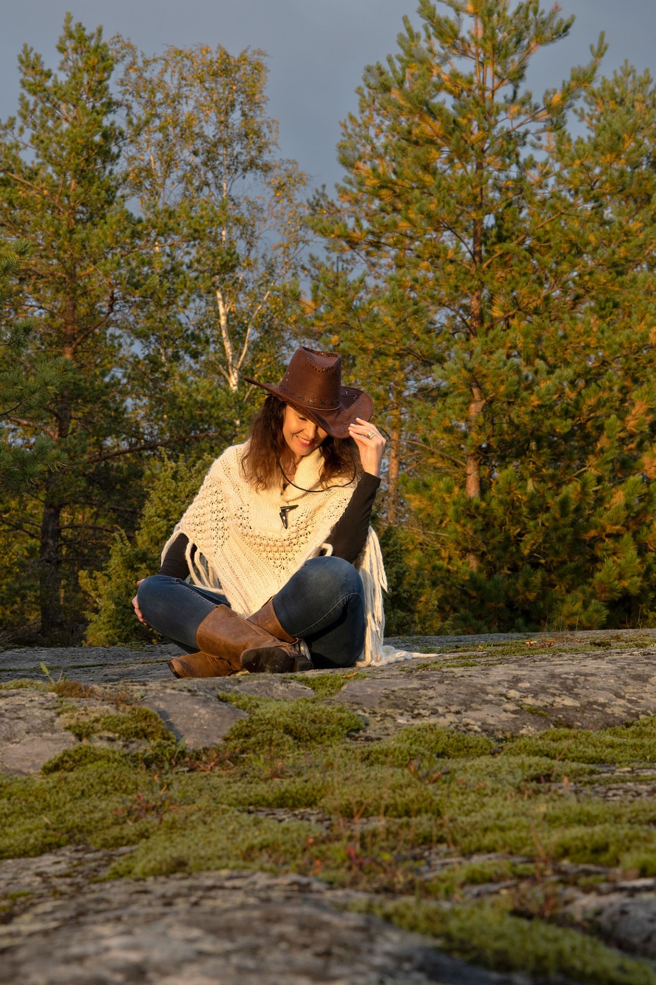 Johanna Rantalainen istuu Kokemäen Orjapaadenkalliolla metsässä, ruskea cowboyhattu päässä, hymyilee ja syksyinen aurinko paistaa.